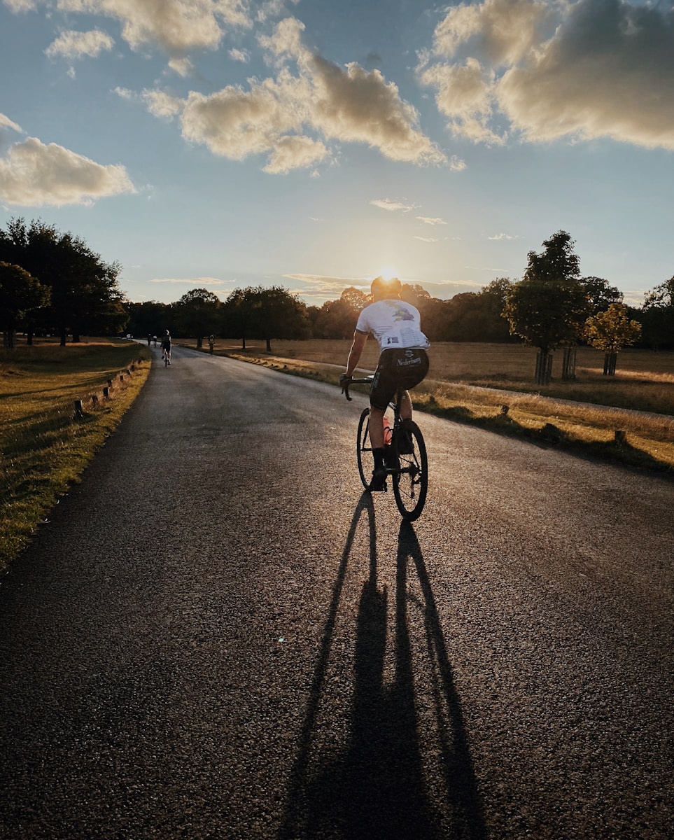 Photo by Hannah Carr man in white shirt riding bicycle on gray asphalt road during daytime